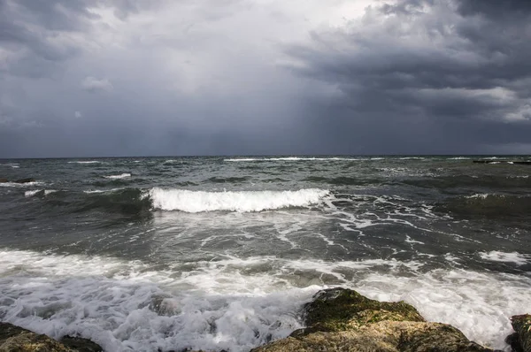 Karadeniz kıyısında küçük dalgalar. Bulutlu gökyüzü gri bulutlar ve beyaz bulutlar. Hafif Rüzgar ve heyecan. Ufuk çizgisi uzaktan görülür.