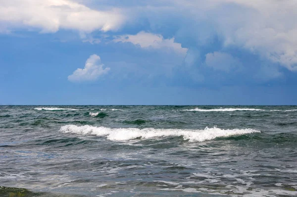 Sea waves with white foam. Beautiful sky and white clouds. The beauty of the sea landscape and nature. Multicolored waves seem calm. Light wind and beautiful seascape