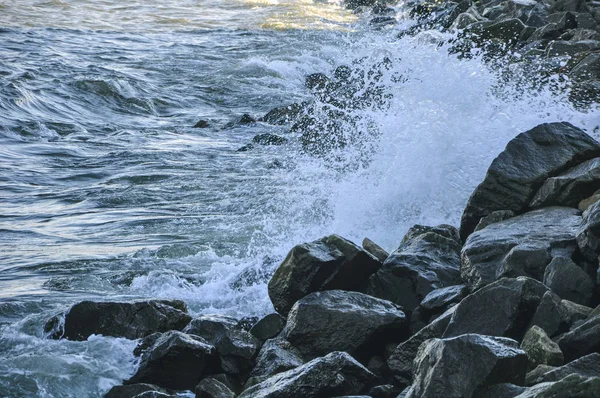 The sea wave. White foamy waves bounce against the stones.