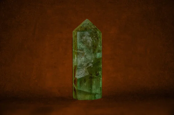 Beryl. Texture of a pyramid of a green stone, on a dark red background. Texture of a stone.. Textures and background.