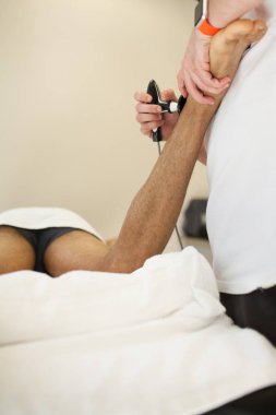 Aşil tendon bir sedyeye baş aşağı ultrason sistemi ile yatan bir adam masaj uygulayarak fizyoterapist