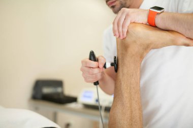 Aşil tendon bir sedyeye baş aşağı ultrason sistemi ile yatan bir adam masaj uygulayarak fizyoterapist