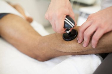 bir sedyeye baş aşağı ultrason sistemi ile yatan bir adam bir ikiz masaj uygulayarak fizyoterapist