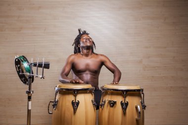 young african rastafarian man enjoys rehearsing and plays the conga, tambourine and cowbell clipart
