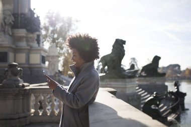 Eğleniyor güzel afro kadın parkta onun akıllı telefon ile iletişim