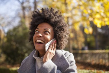 Eğleniyor güzel afro kadın parkta onun akıllı telefon ile iletişim
