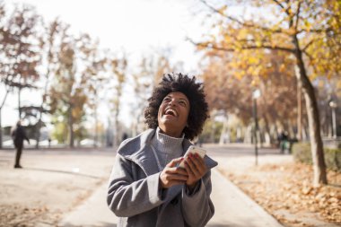 Eğleniyor güzel afro kadın parkta onun akıllı telefon ile iletişim