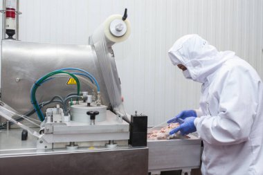 Hijyenik iş elbiselerine sahip bir işçi et kesme odasının koruyucu atmosfer paketleme makinesini kullanıyor.