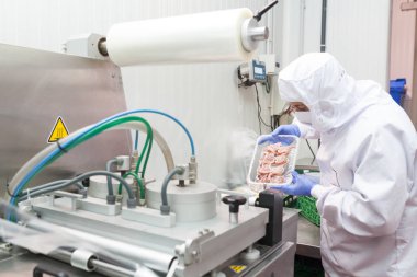 Hijyenik iş elbiselerine sahip bir işçi et kesme odasının koruyucu atmosfer paketleme makinesini kullanıyor.