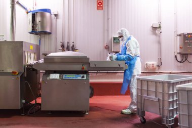 Et doğrama odasının vakum paketleme makinesini kullanarak hijyenik giysiler giyen bir işçi.