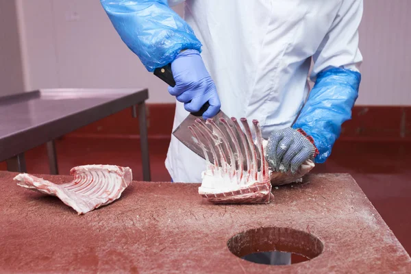 Meat cutting room worker preparing a rack of lamb
