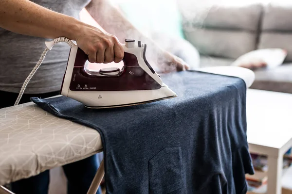 unrecognizable woman ironing clothes on the ironing board at home