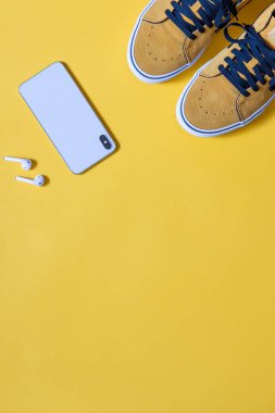 dikey model, sarı arka planda hardal renkli ayakkabılar, akıllı telefon ve kulaklıklar, kopyalama alanı
