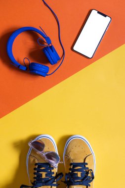 dikey model, hardal rengi ayakkabılar iki renk sarı ve turuncu arka plan, beyaz ekran ve kulaklıklı akıllı telefon, kopyalama alanı