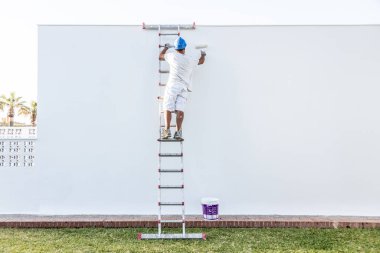 Tanımlanamayan genç bir ressam apartman cephesini boyuyor, merdivenleri tırmanıyor.