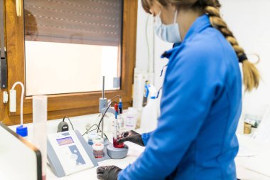 Şarap mahzeninin laboratuarında saflık ve şarap örneklerini kontrol eden genç bir kadın teknisyen.