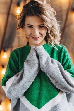 Modern gülümseyen sarışın kadın yeşil kazaklı ışıklar duvar çerçevede bir closeup portresi