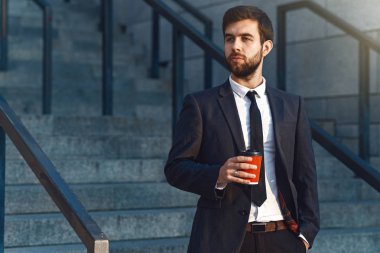 Takım elbiseli genç işadamı closeup elinde tutan bir kırmızı kağıt bardak kahve ve ofisinin sabah erkenden içmeye gidiyor. Offee ara, arka plan bulanık.