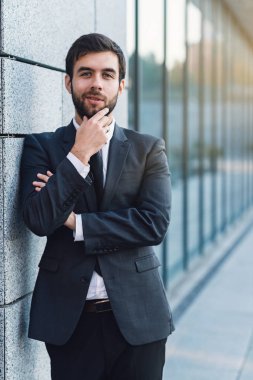 Duvara yaslanmış ofis binası arka plan üzerinde poz takım elbiseli bir sakal tutan genç işadamı portresi