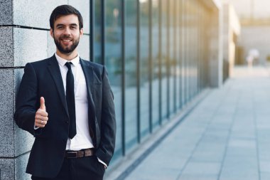 Ofis duvara yakın binası arka plan üzerinde poz yukarı başparmak gösterilen gülümseyen işadamı portresi