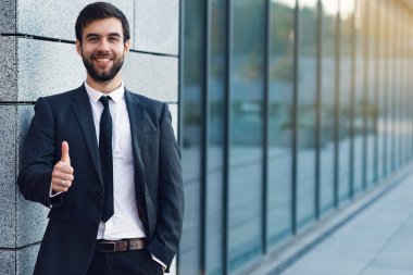Ofis duvara yakın binası arka plan üzerinde poz yukarı başparmak gösterilen gülümseyen işadamı portresi