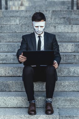 Onun yüzünde maske ile işadamı laptop içine görünüyor. Bir iş kurma açık belgili tanımlık merdiven üstünde oturuyor