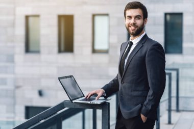 Takım elbiseli neşeli işadamı yaygın gülümsüyor. Office bir dizüstü bilgisayar ile arka planda duruyor. Açık