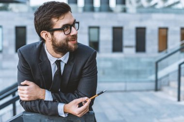 Gözlük iş takım elbiseli adam bir kalem bir ofis binasının arka planı elinde tutar. Yan açık bak