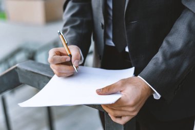 Takım elbiseli genç işadamı kalem ve temiz beyaz kağıt tutar. Arka plan bulanık