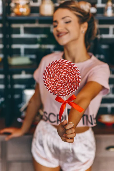 Pembe el ileri lolipop üzerinde mutfakta sarışın bir kadın. Lolipop yakın kadar arka plan bulanık