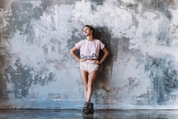 Modern woman in pink pajamas and slippers stands against the background of an abstract drawing of a wall