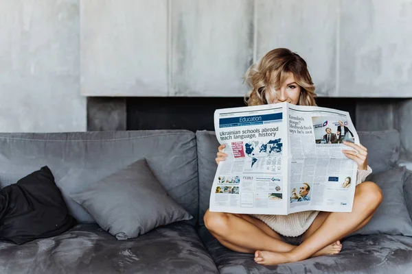 年轻性感的金发女孩坐在沙发上拿着报纸 — 图库照片