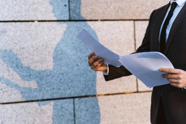 Close-up businessman  in a classic suit reading advantageous business document in paper form. Outdoors a man and his shadow on the wall of a building.