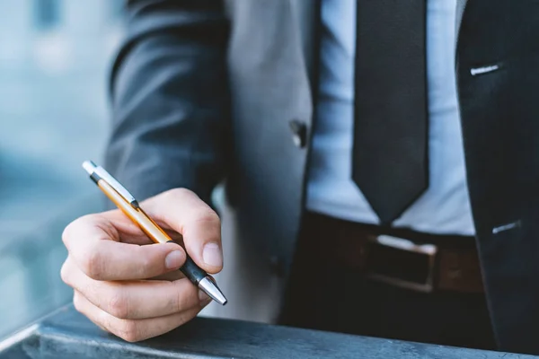 Man in a business suit holds a pen in his hand. Blurred background