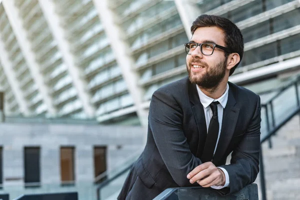 Portrait of a young man businessman with eyeglasses against the background of an office building with glass facades. Look sideway and up