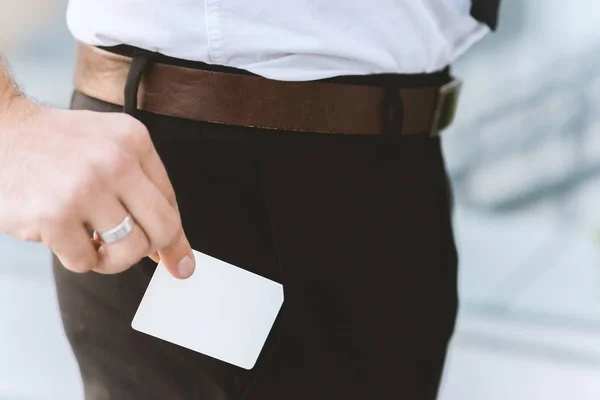 Male hand with white empty business card near pocket, close-up photo with selective focus. Horizontal placement