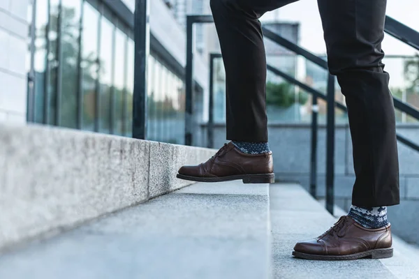 lose up of male legs in business trousers and shoes walking up the stairs of a business building