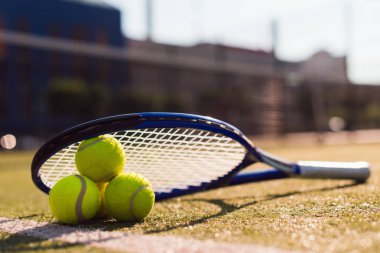 Güneş ışığı altında sert kortta üç tenis topu ve raket