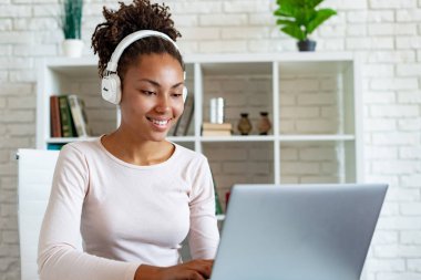 Kulaklıkdizüstü üzerinde çalışan ve müzik dinleyen mutlu bir mulatto kadın freelancer Portresi