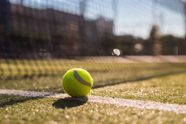 Pelota de tenis acostada en línea blanca en pista dura bajo la luz del sol — Foto de Stock