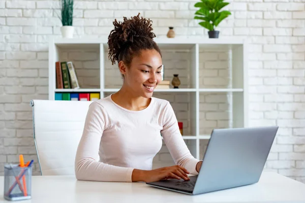 Mulatto kobieta pracuje na laptopie w biurze patrząc na ekranie i wpisując. -Obraz — Zdjęcie stockowe