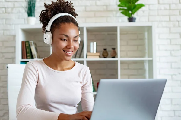 Kulaklıkdizüstü üzerinde çalışan ve müzik dinleyen mutlu bir mulatto kadın freelancer Portresi