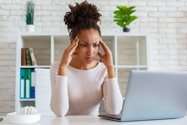 Mulatto woman have a chronic headache, touching temples to relieve pain during working on laptop — Stock Photo, Image