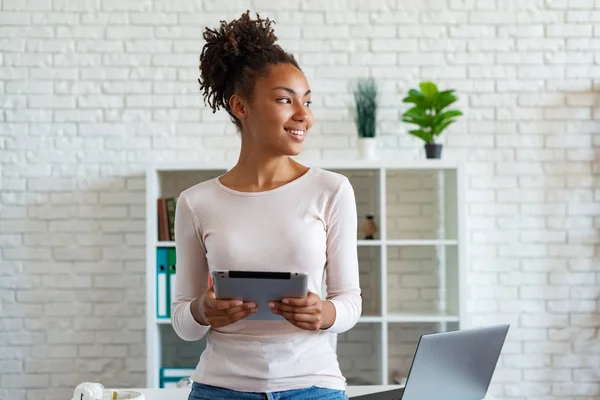 Pretty mulatto kadın ofiste bir dinlenme var, bir tablet tutan masaya eğildi ve rüya gibi bakıyor