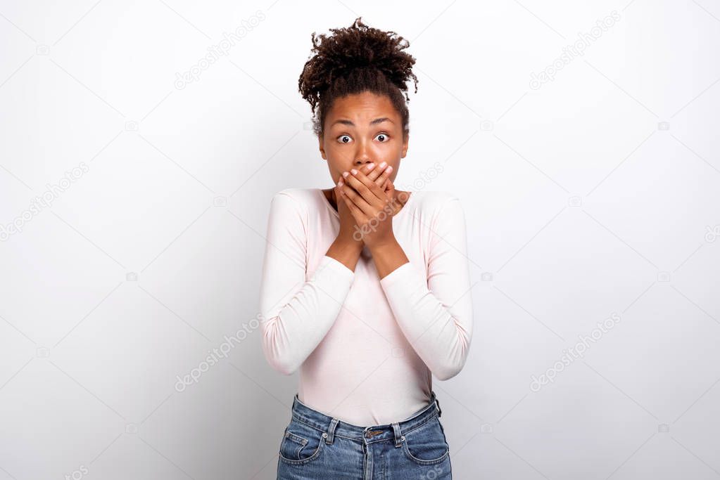 Shocked woman shut mouth with her arms looking at the camera, feel amazed on ligth-grey studio background