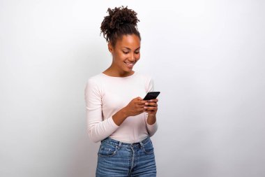 Yakışıklı mulatto kadın bir ligth stüdyo arka plan karşı ekrana bakarak cep telefonu tutarak duruyor