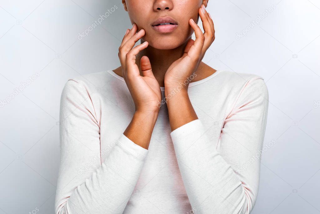 Cropping closeup portrait of a beautiful serious mulatto girl over light background touches herself face - Image