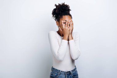 Yüzünü beyaz arka planda örten korkmuş bir kadının resmi.