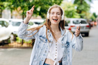 Havalı, genç bir kız, caddenin ortasında kulaklıkla müzik dinlerken dans ediyor.