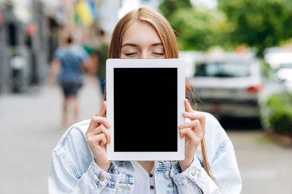 一个积极的女孩在街上展示一个空白的平板屏幕的前视图画像 — 图库照片